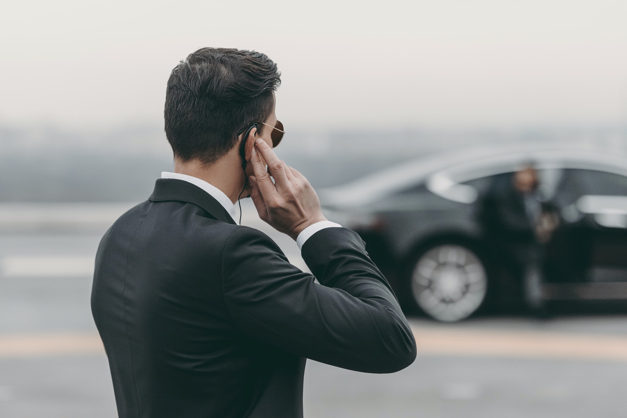 handsome bodyguard standing and listening message with security earpiece on helipad - Vadium Security